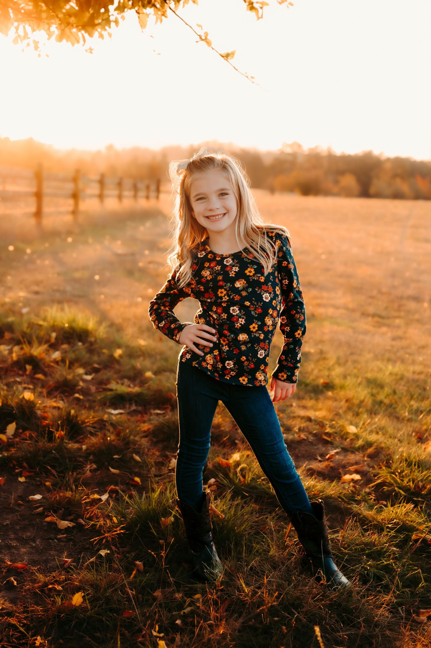 Child playing in golden sunlit field wearing floral top and jeans at sunset.