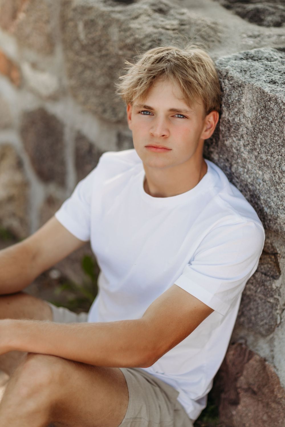 Summer portrait of person in white t-shirt sitting against stone wall.
