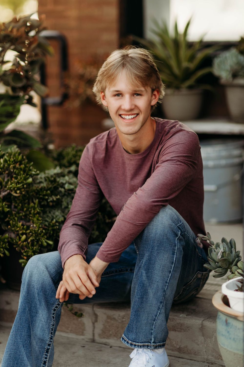 Casual portrait of person in burgundy sweater sitting outdoors among potted plants.