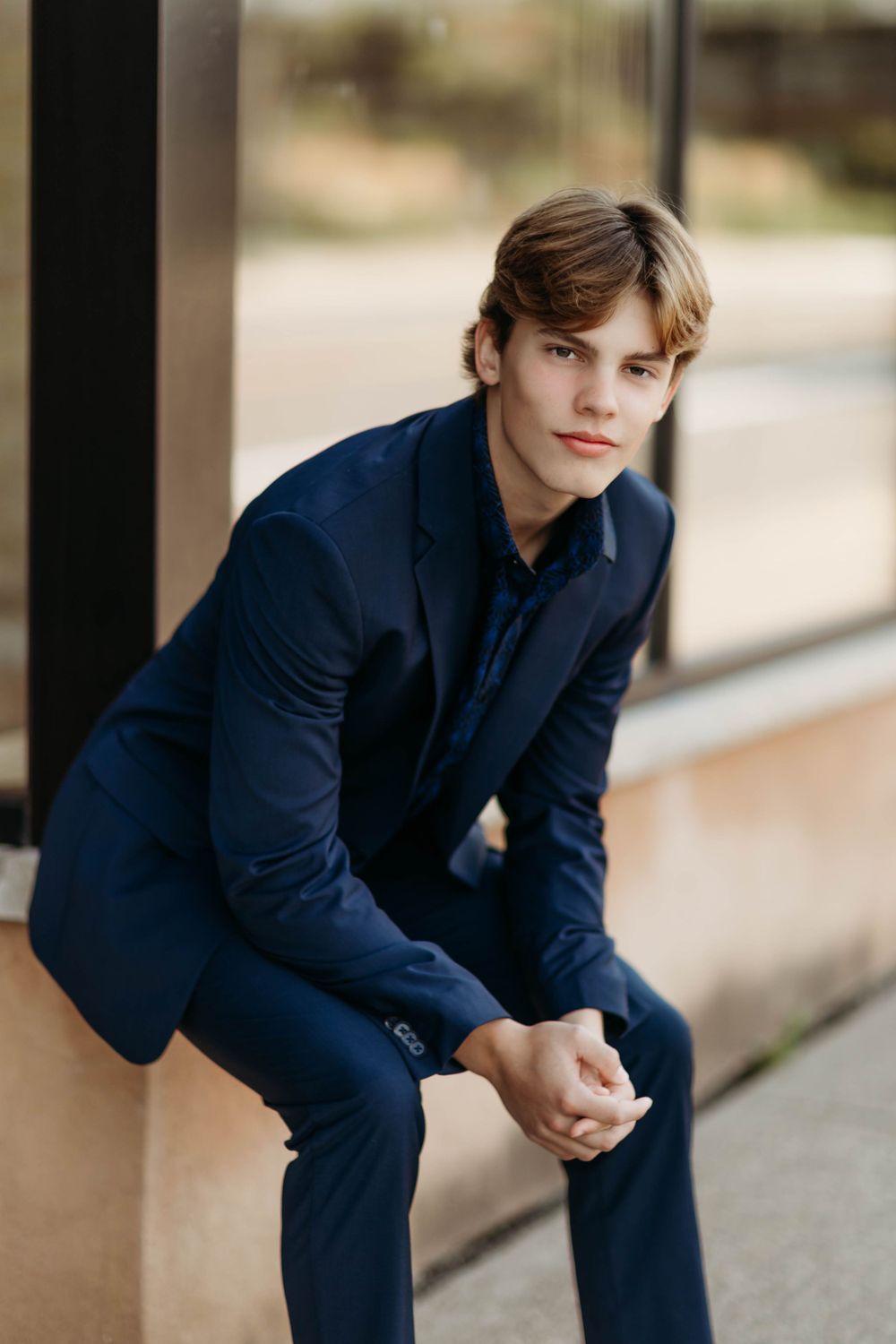 Stylish portrait of someone in a navy blue suit sitting on steps.