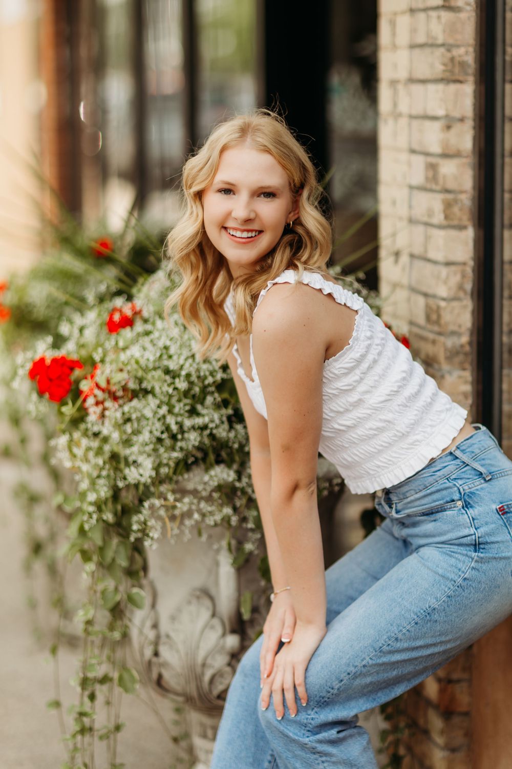 Casual portrait by brick wall with flowers wearing jeans and white top.