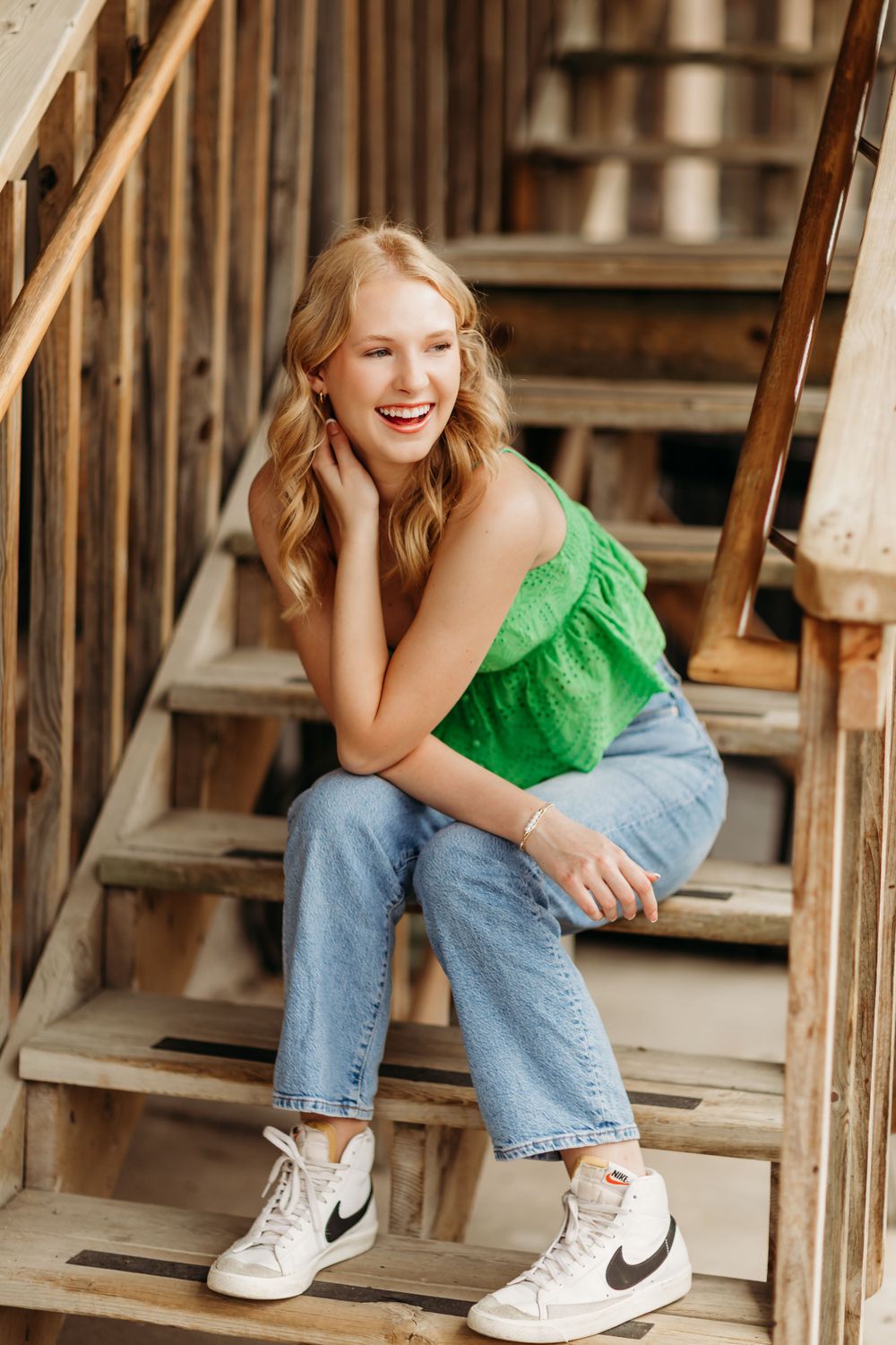 Casual portrait on wooden stairs wearing green top and jeans with Nike sneakers.