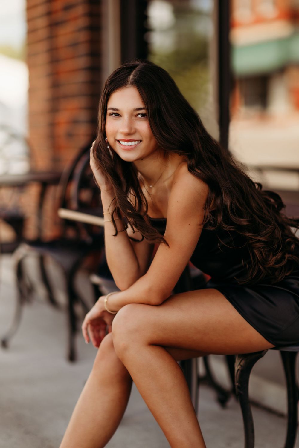 Portrait of a person in black dress sitting outdoors with long dark hair.