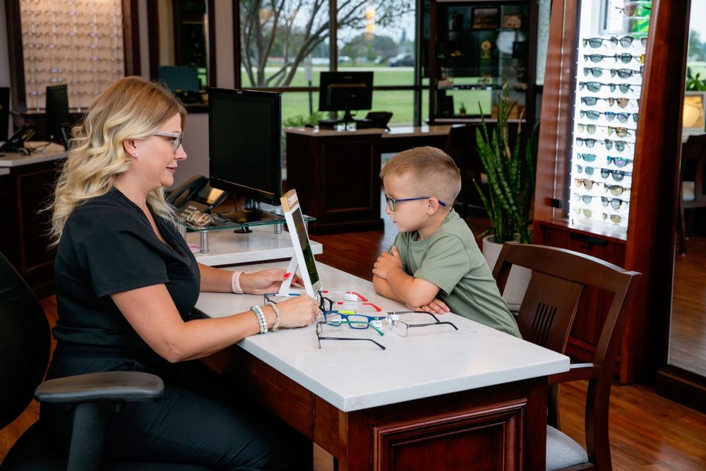 Optical staff member helping young customer select eyewear at consultation table.