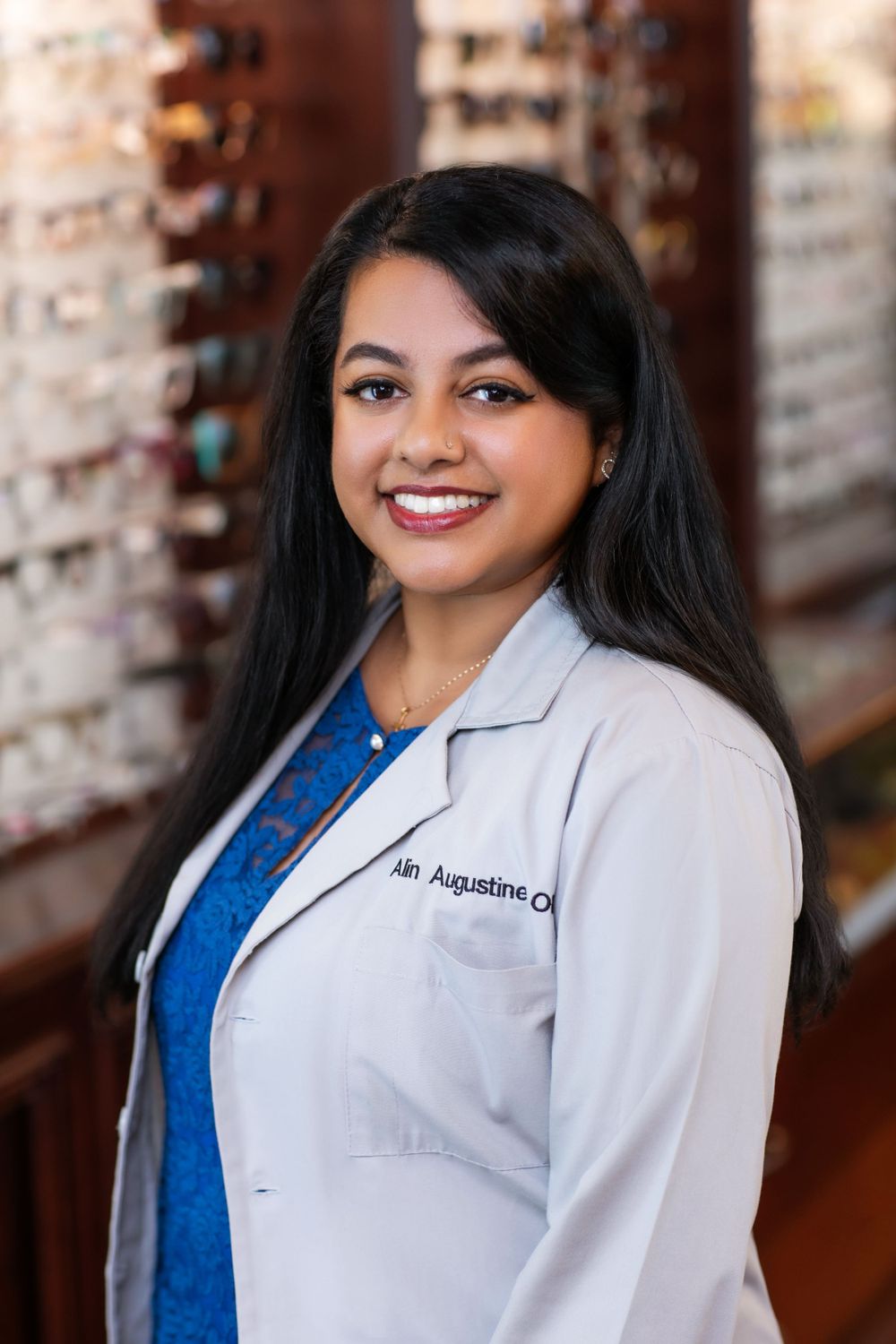 Professional headshot of optometrist in white coat standing in optical store.