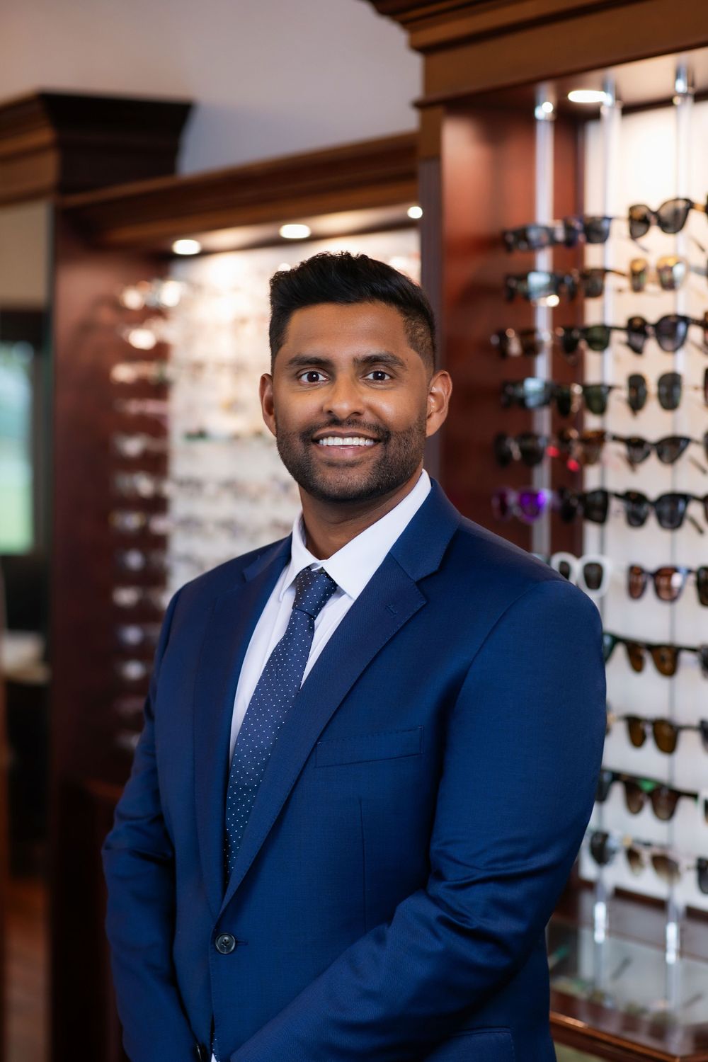 Professional portrait of eye care specialist in navy suit standing in optical store.