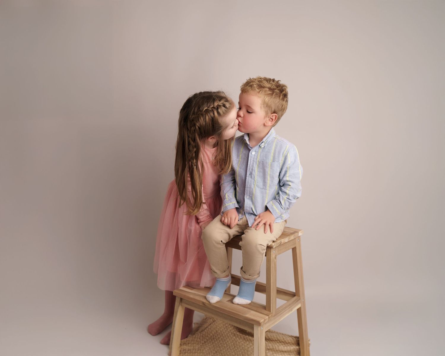 Candid studio portrait moment on wooden steps with neutral background.