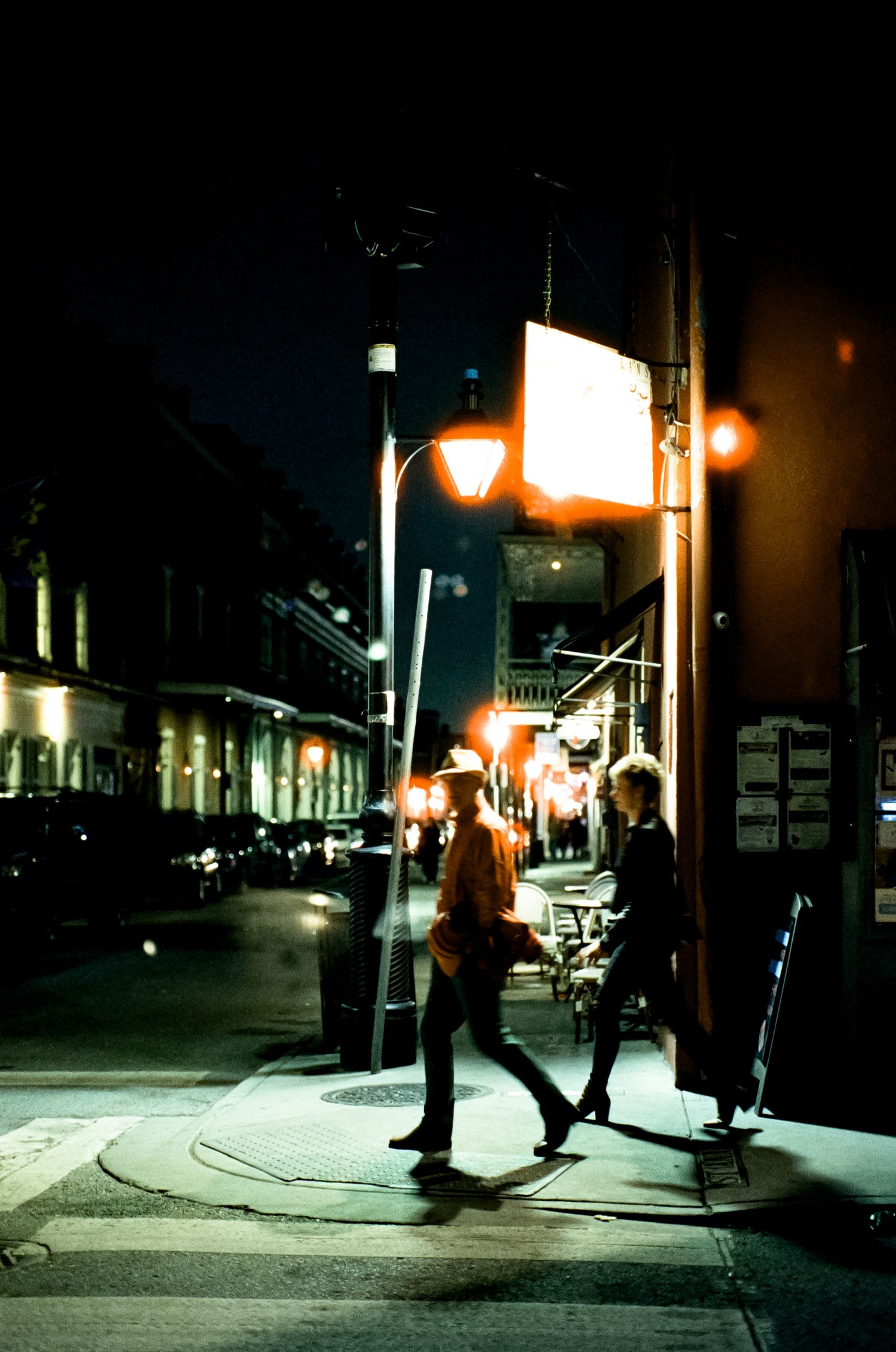 People walking under streetlights on a dark urban street corner at night.