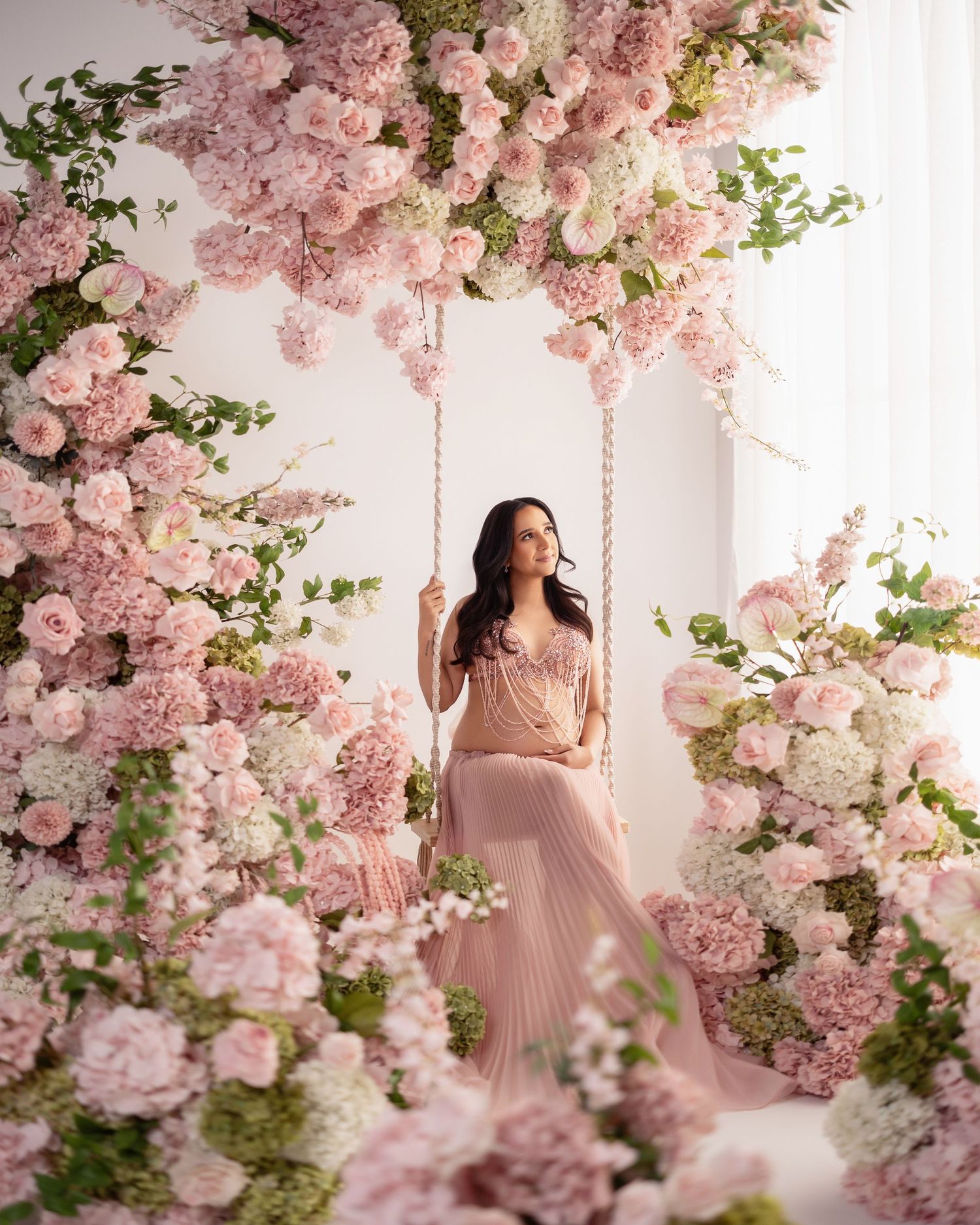 Romantic maternity photoshoot in a dreamy setting with pink cherry blossoms and white flowers creating an ethereal atmosphere.