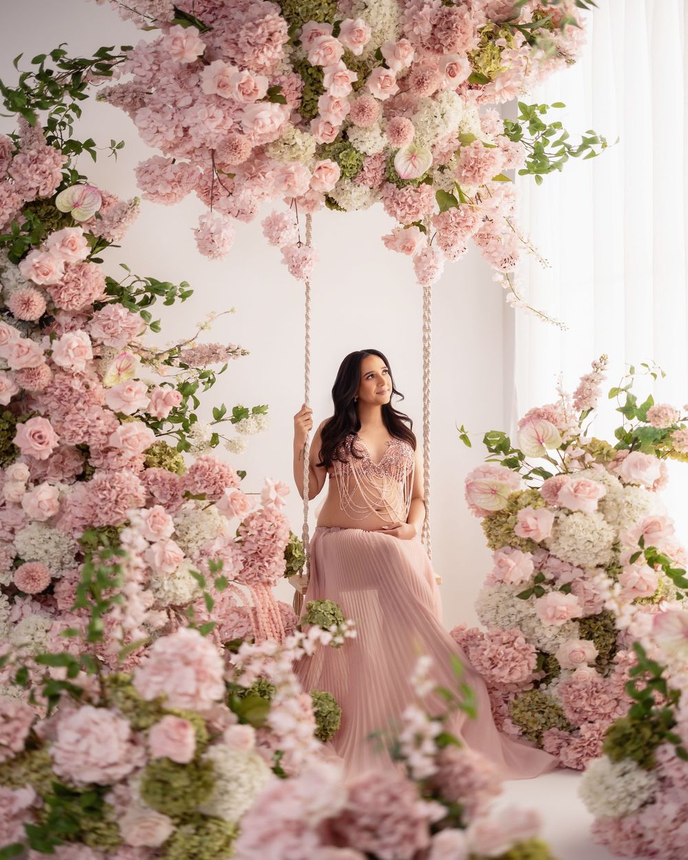 Romantic maternity photoshoot in a dreamy setting with pink cherry blossoms and white flowers creating an ethereal atmosphere.