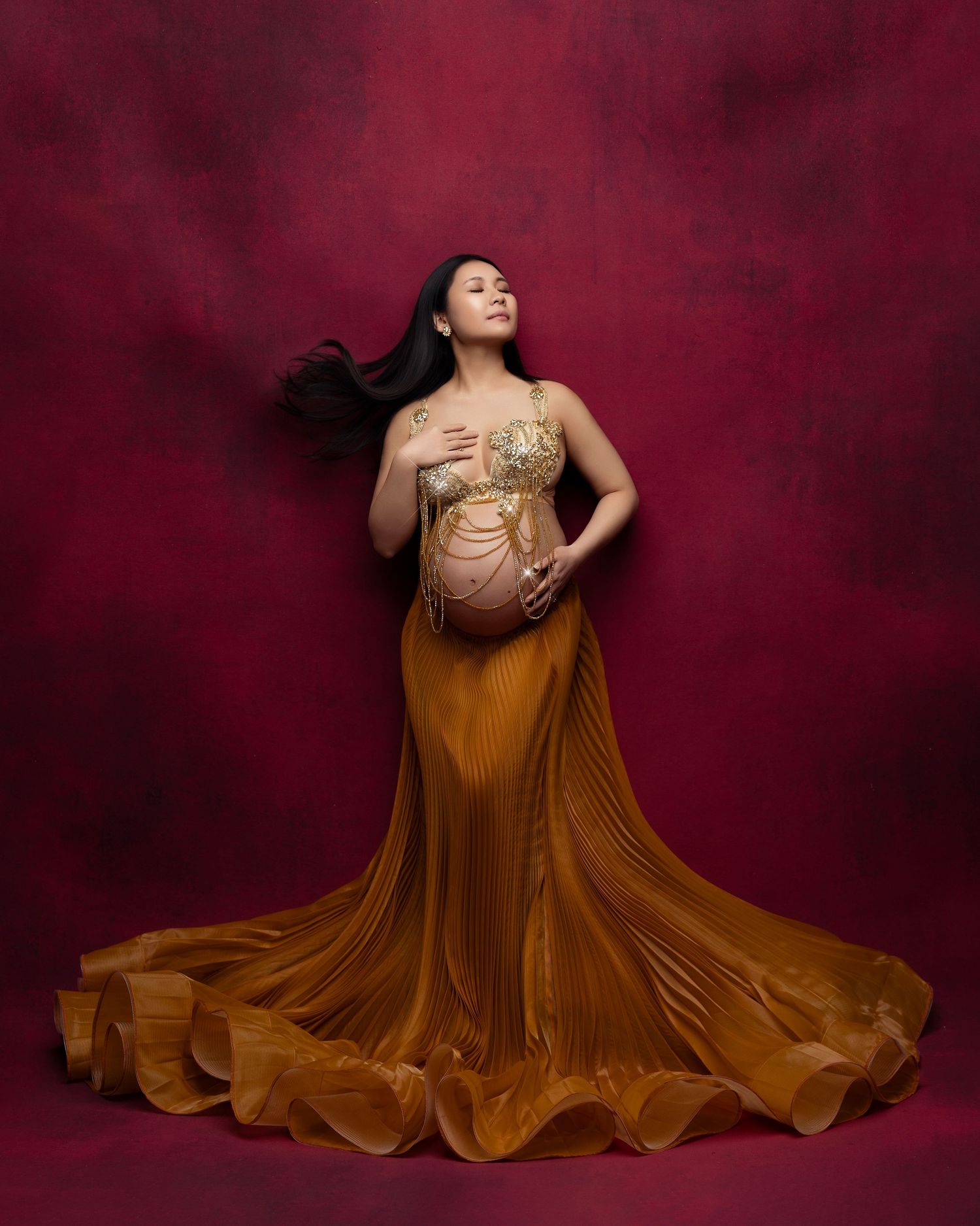A figure in a flowing copper-colored gown poses dramatically against a deep burgundy backdrop in a dynamic photoshoot series.