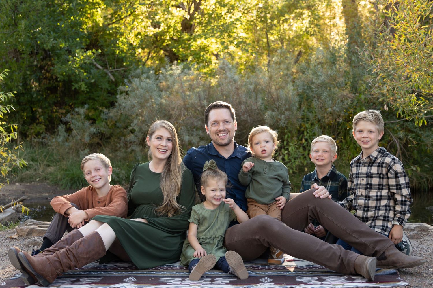 A family sits together on a blanket in a natural outdoor setting during golden hour.
