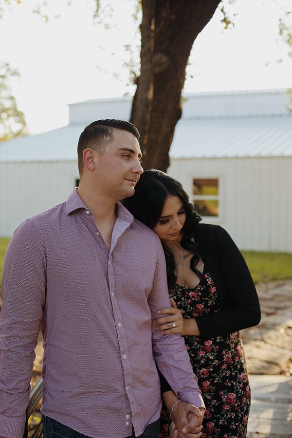 Couple interlocking arms and staring off into the distance on a bridge over a river.