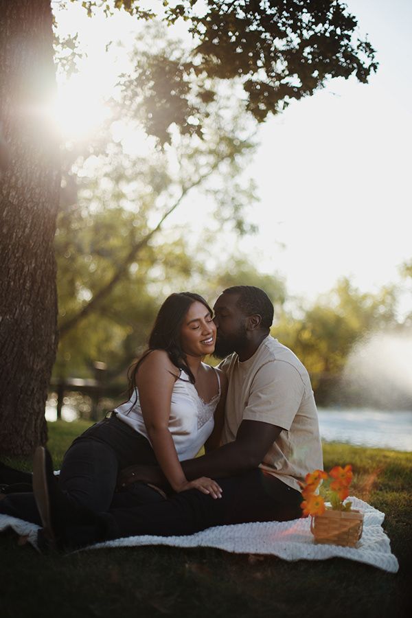 Engaged couple kissing on the grass near a pond.