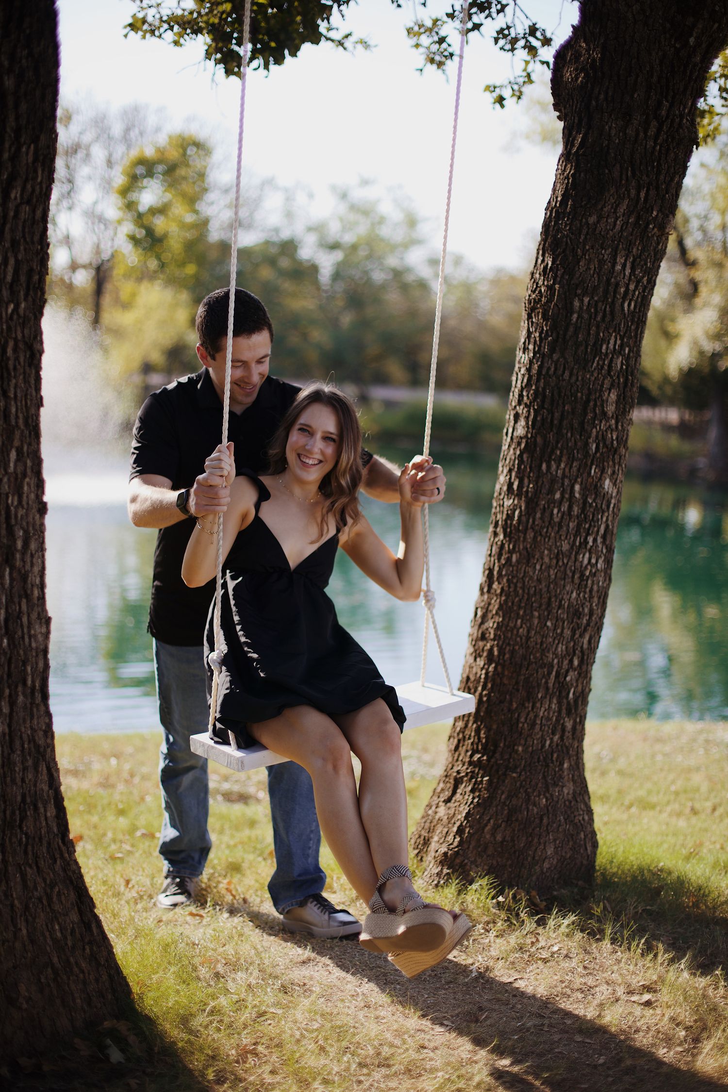 Fiance being pushed on a swing near a pond.