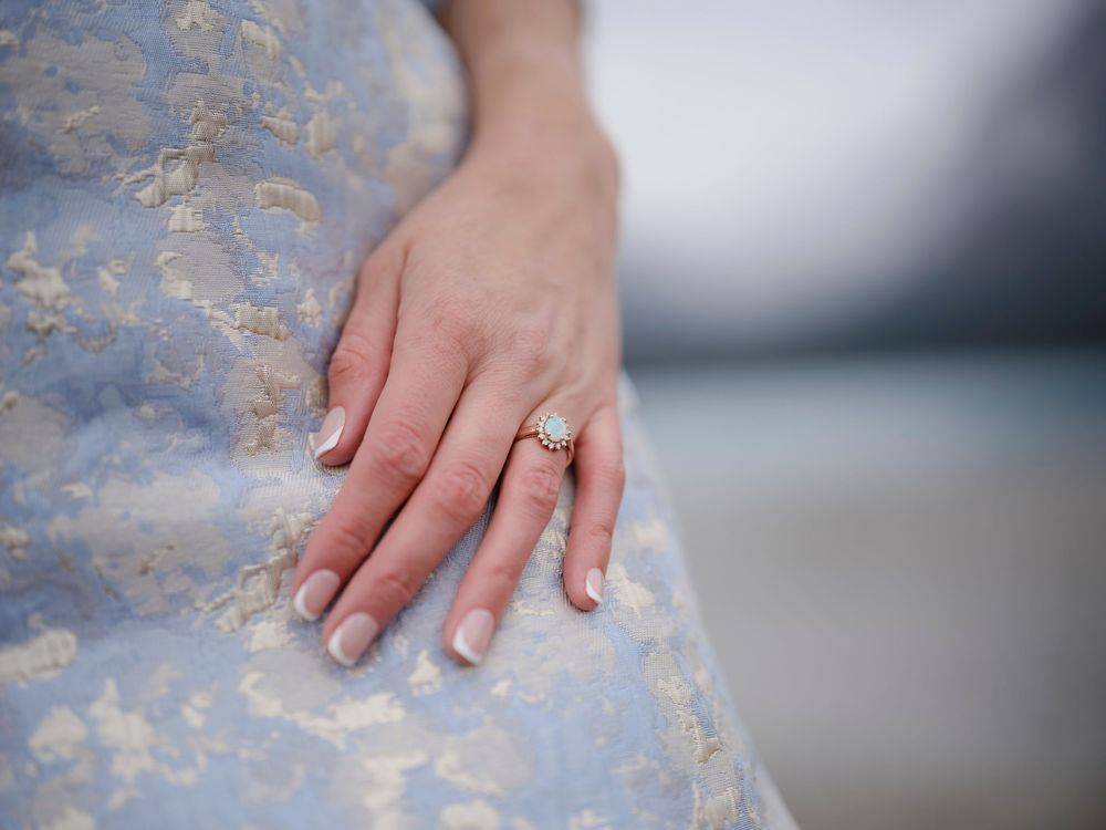A hand wearing an engagement ring is shown against a light blue floral background in Banff by a lake