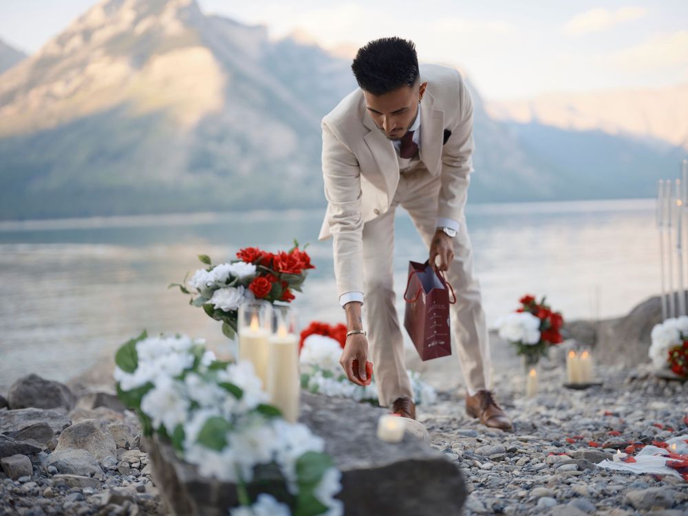 A couple celebrates their wedding ceremony on a rocky beach at sunset with mountains and lake in the background in Banff