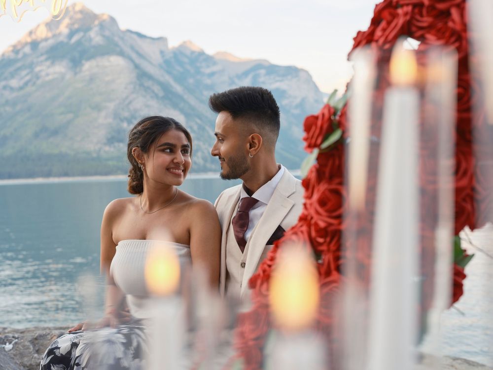 A romantic couple shares an intimate moment by a scenic mountain lake at sunset with glowing lanterns in the foreground in Banff
