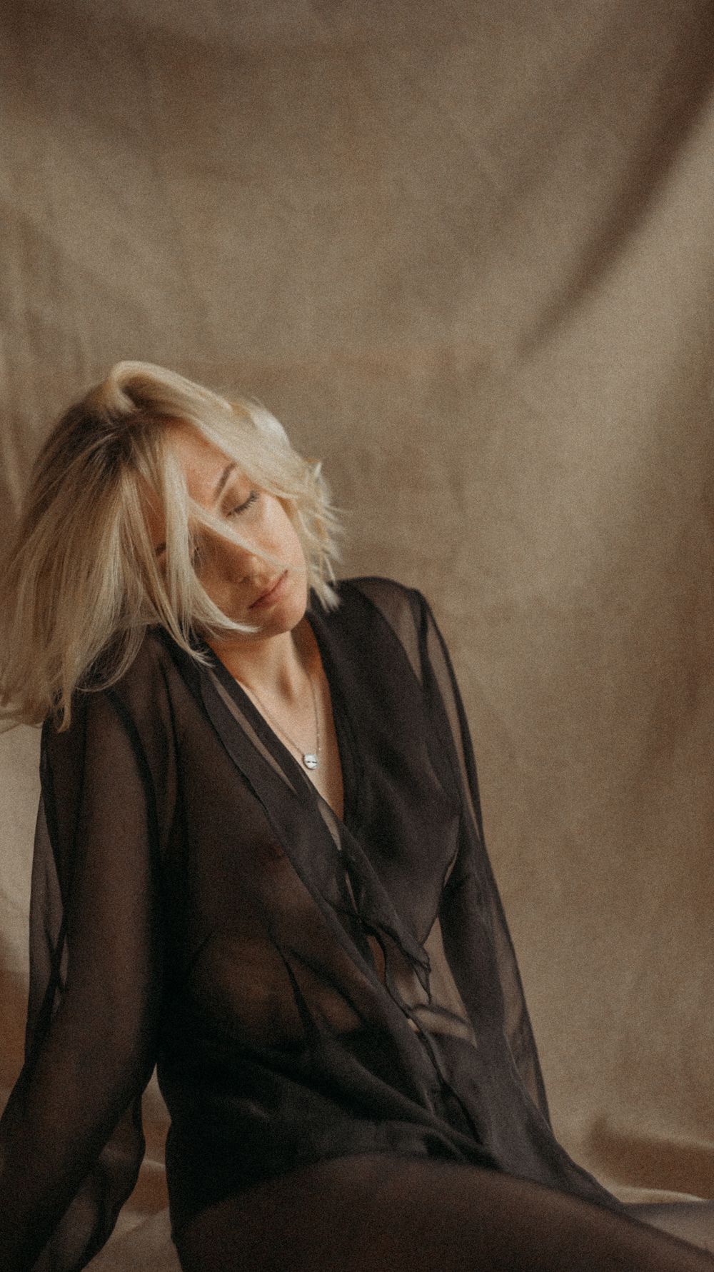 Woman in black blazer poses artistically against neutral backdrop.