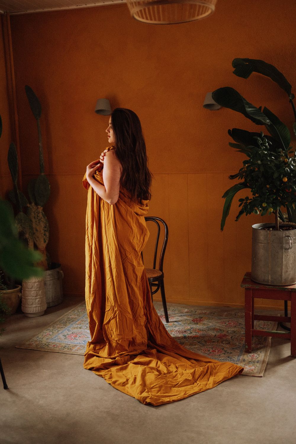 Artistic portrait series with mustard yellow fabric against terracotta walls.