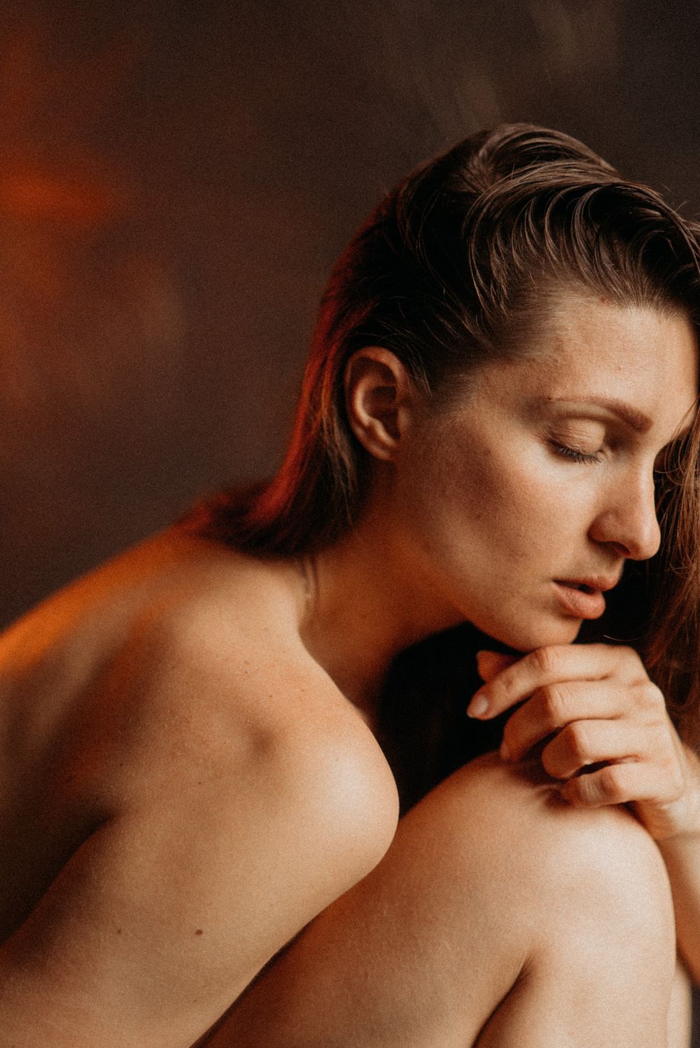 Intimate portrait with warm lighting showing contemplative pose against dark background.