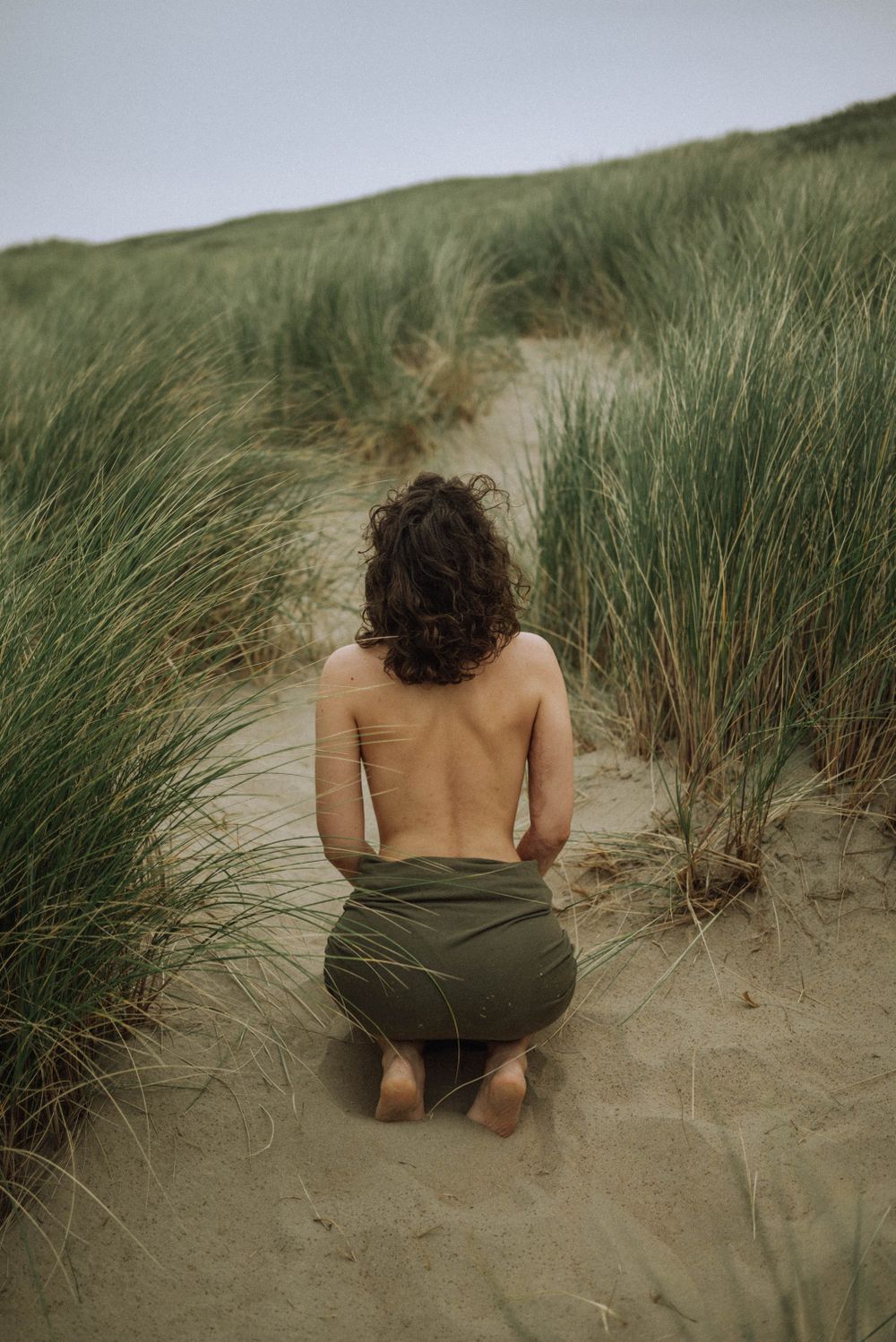 Person sitting among beach grass dunes in muted tones.