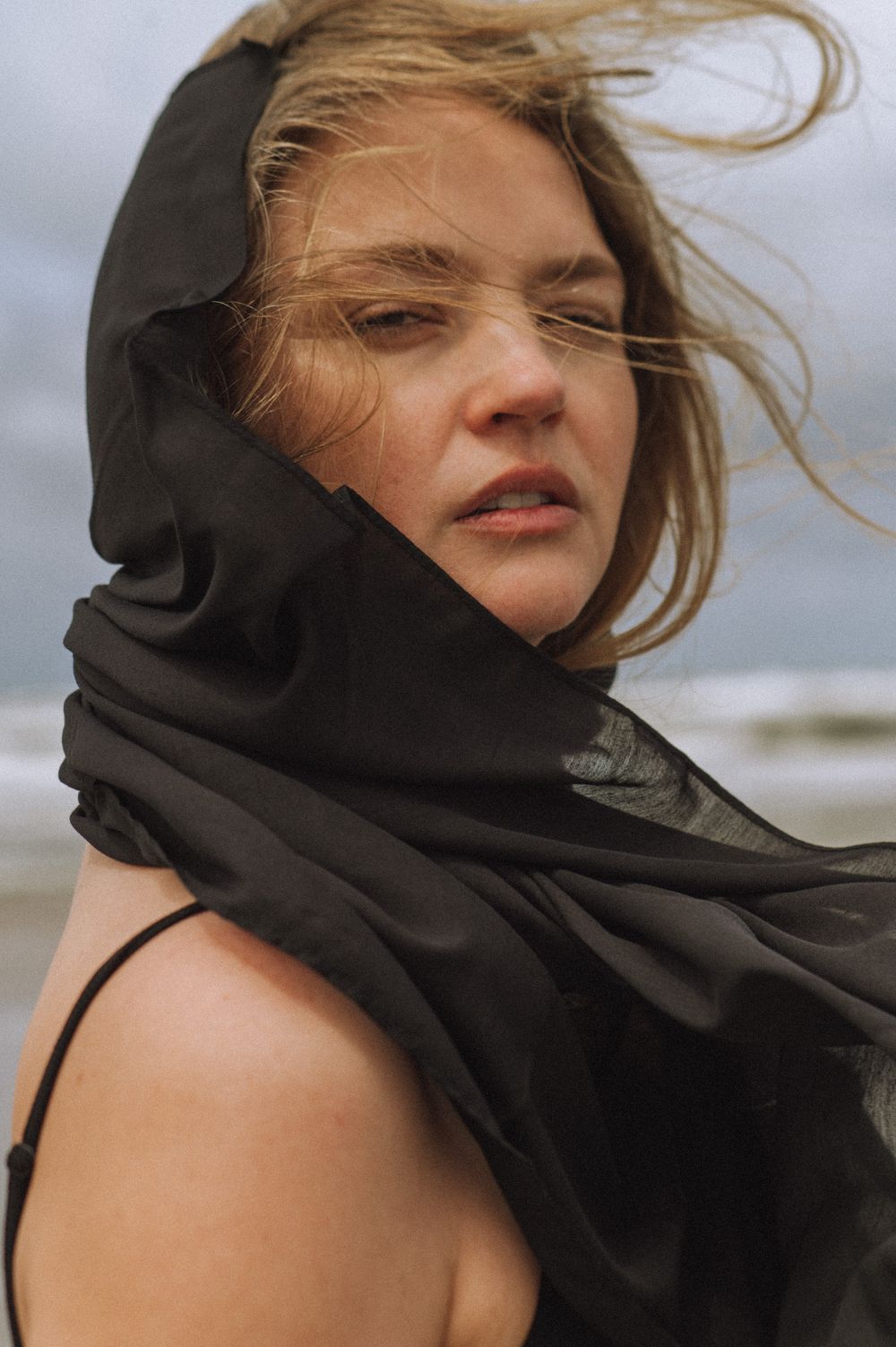 Windswept portrait on a beach with black fabric dramatically framing the shot.