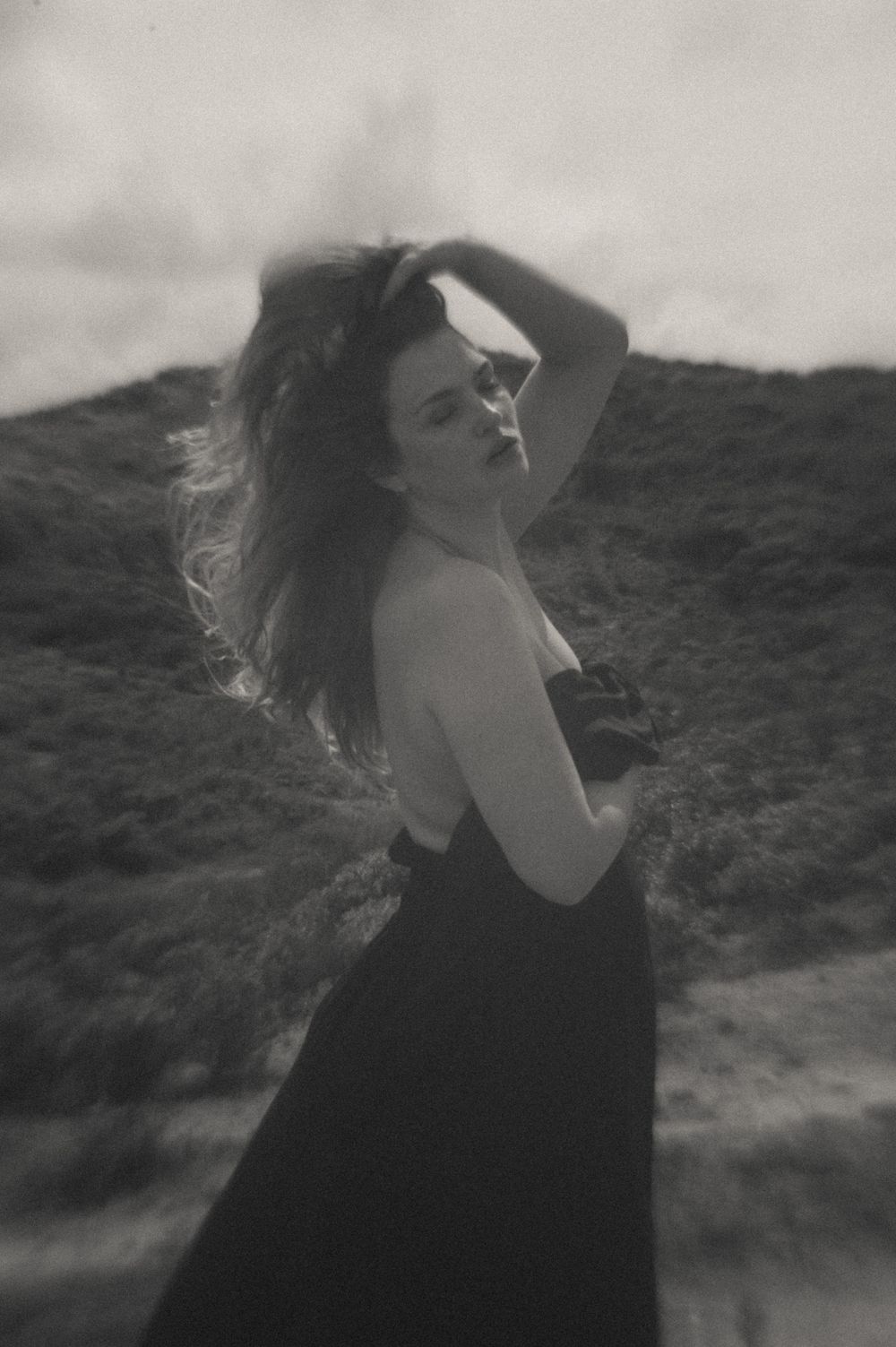 Artistic black and white photos of a figure with windswept hair against a hillside.