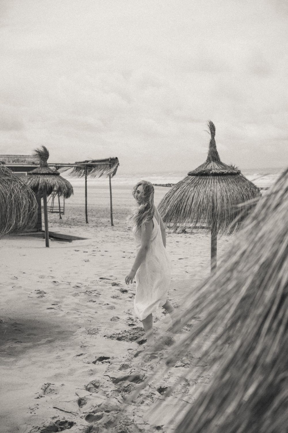 Beach scene with thatched umbrellas and a flowing white dress caught in the wind.