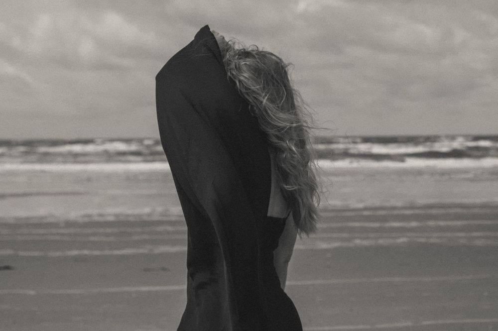 Silhouetted figure against dramatic ocean waves and cloudy sky.