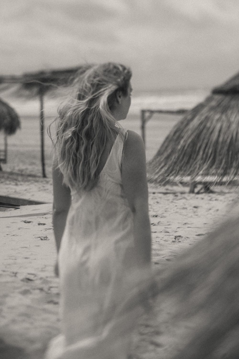 Wind-swept beach scene with thatched umbrellas and flowing fabric in black and white.