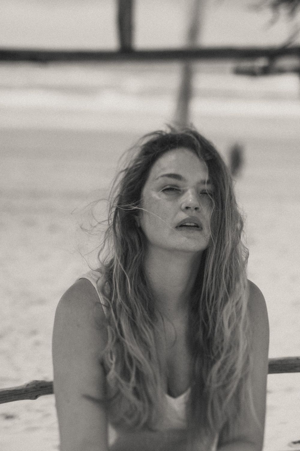 Black and white portrait series showing a woman with tousled hair lying on a beach.