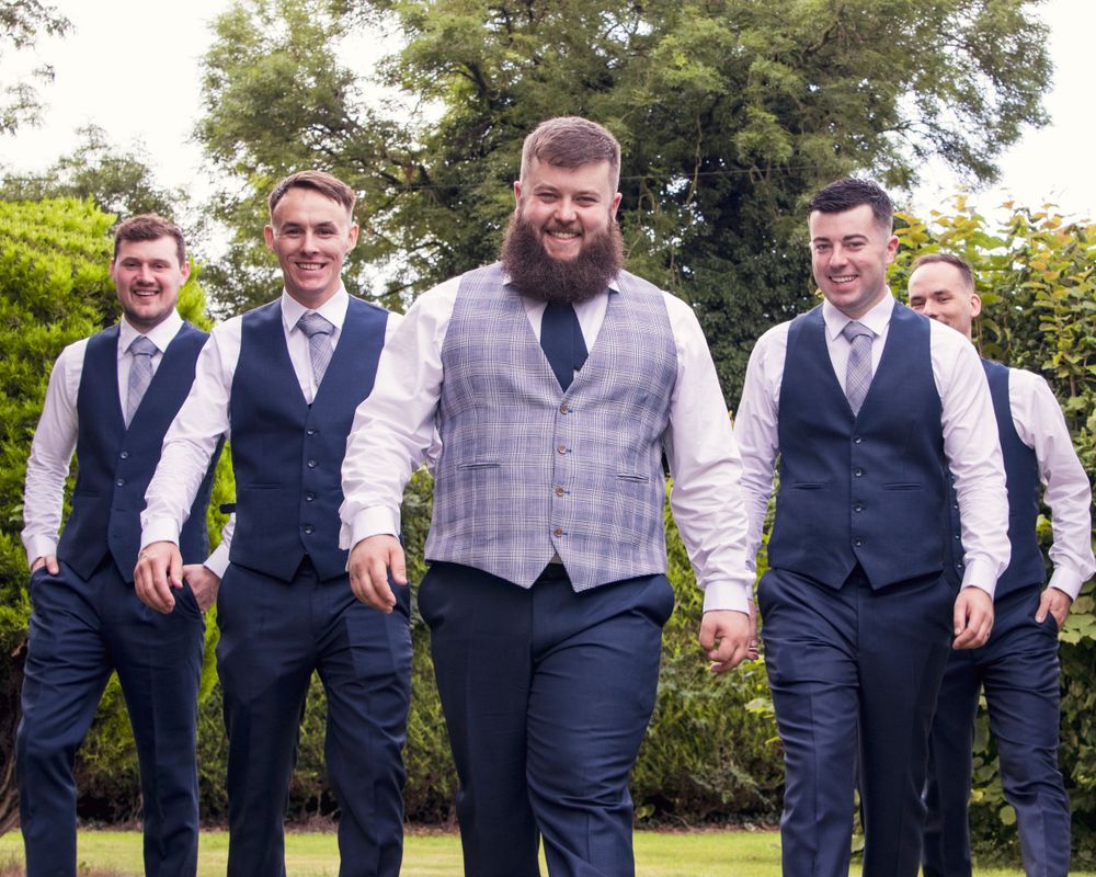 Wedding party in navy suits and vests posing casually outdoors.
