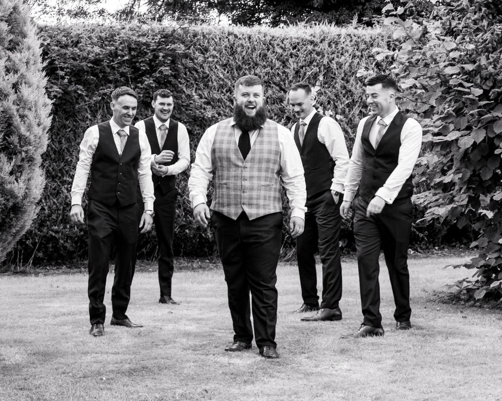 Group of formally dressed groomsmen walking outdoors in black and white photography.