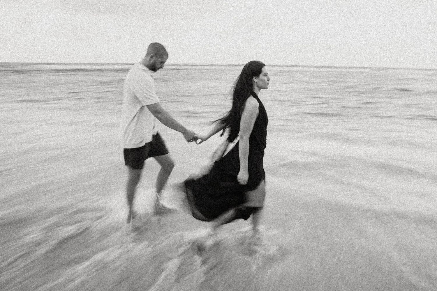 Two people play in ocean waves at sunset, creating silhouettes against the water's reflective surface.
