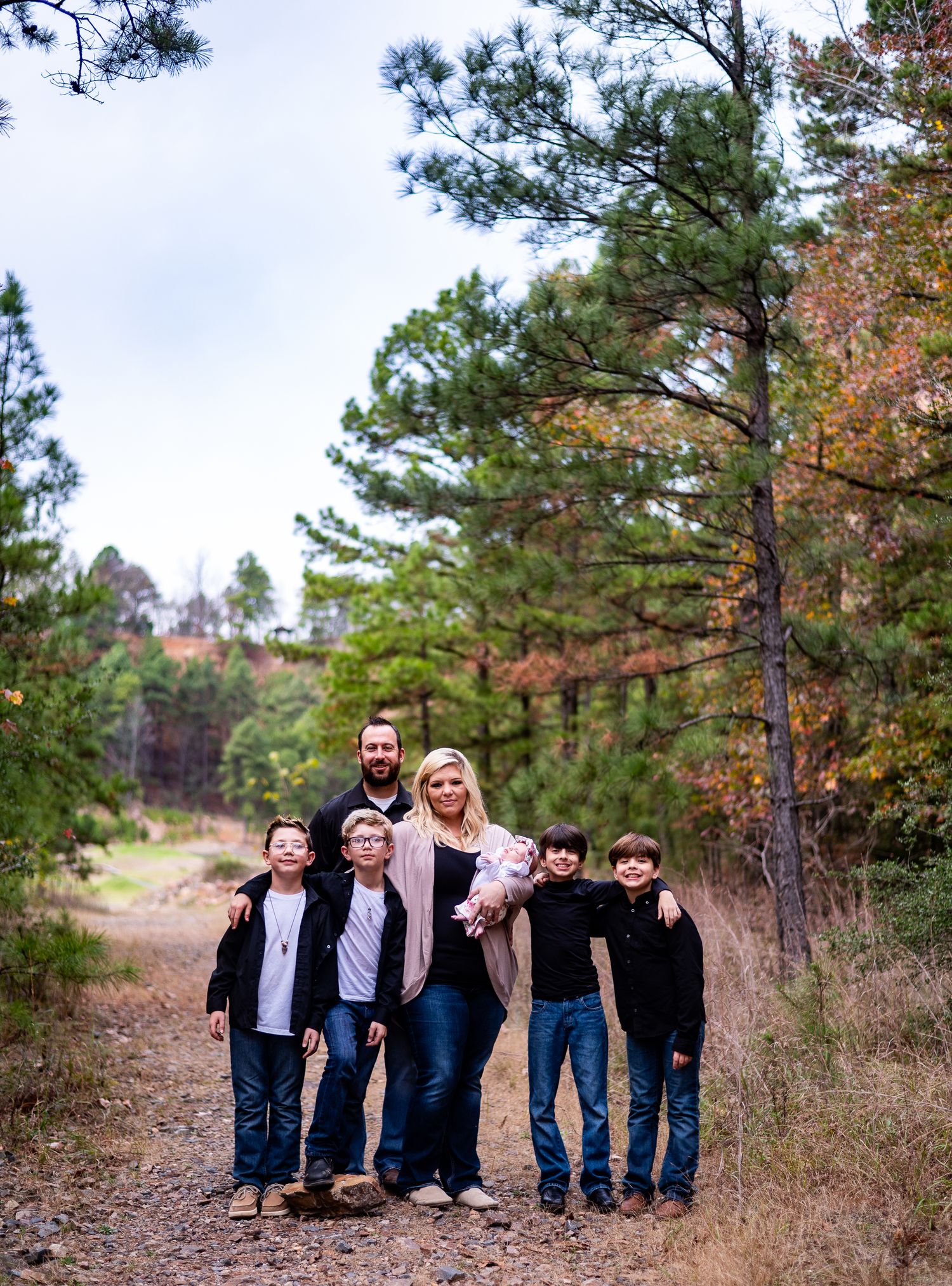 Family of six posing on a forest trail surrounded by pine trees during autumn for an outdoor family portrait.
