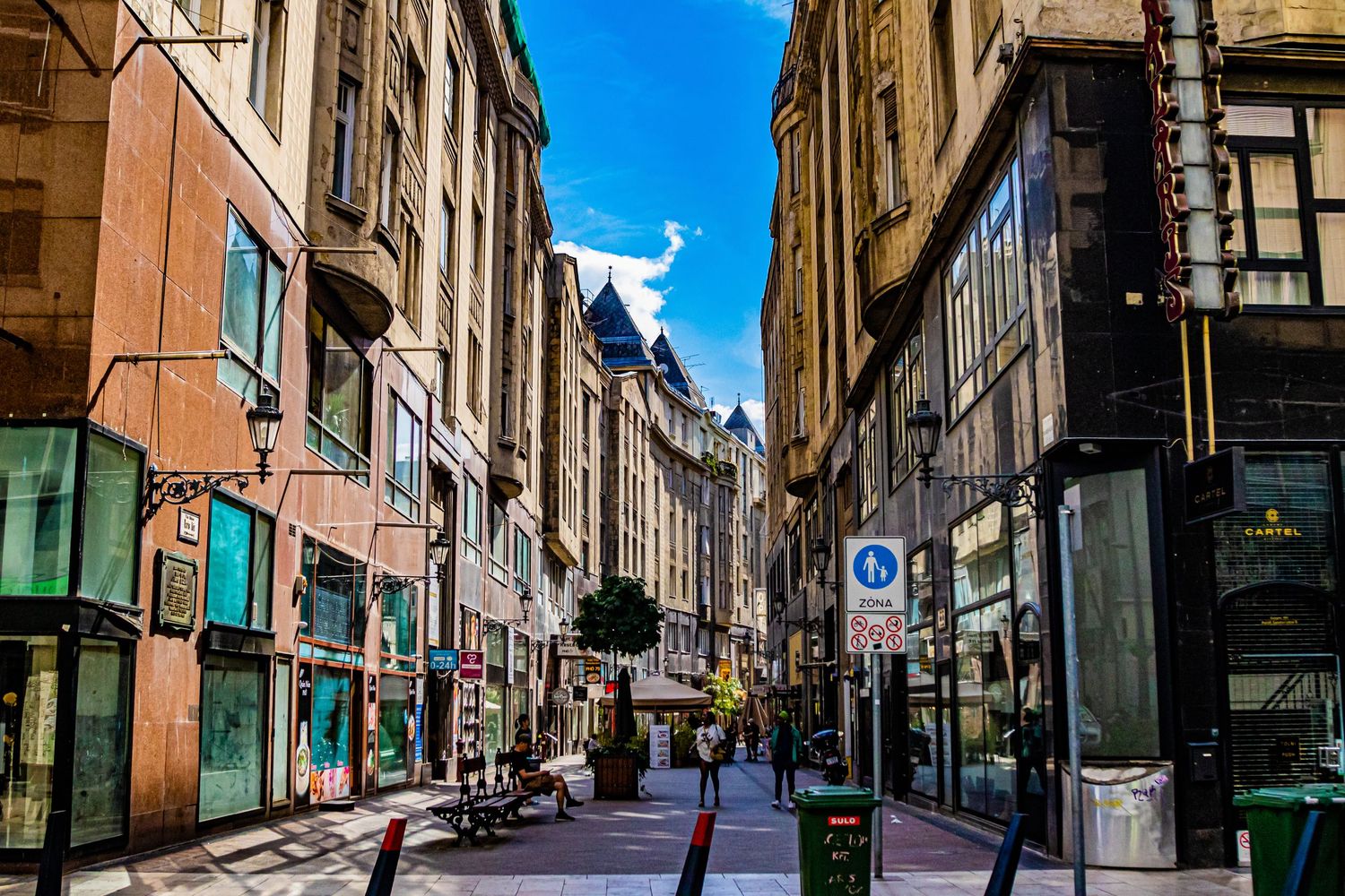Historic European street lined with classical architecture and shops under bright blue skies.