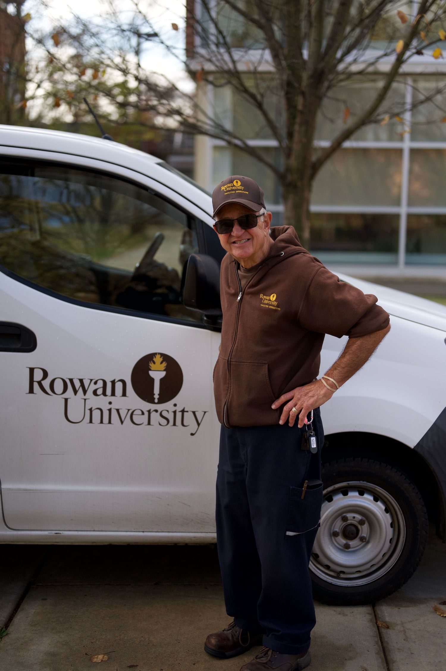 A Rowan University employee stands next to a branded white university vehicle.