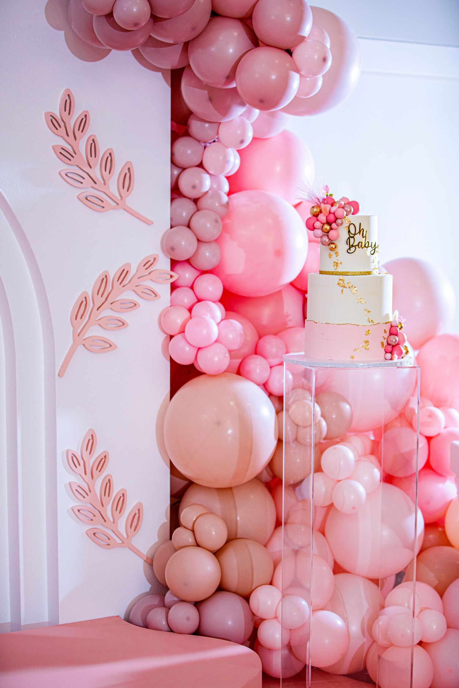 Pink balloon arch with floral accents and tiered cake for elegant party decoration.