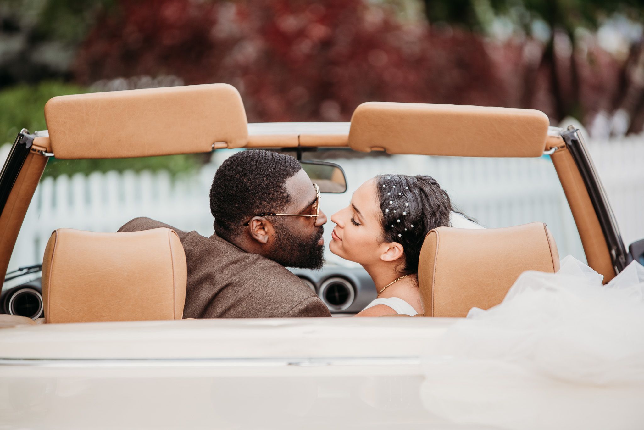 Romantic couple sharing an intimate moment in a vintage convertible car with tan leather seats.