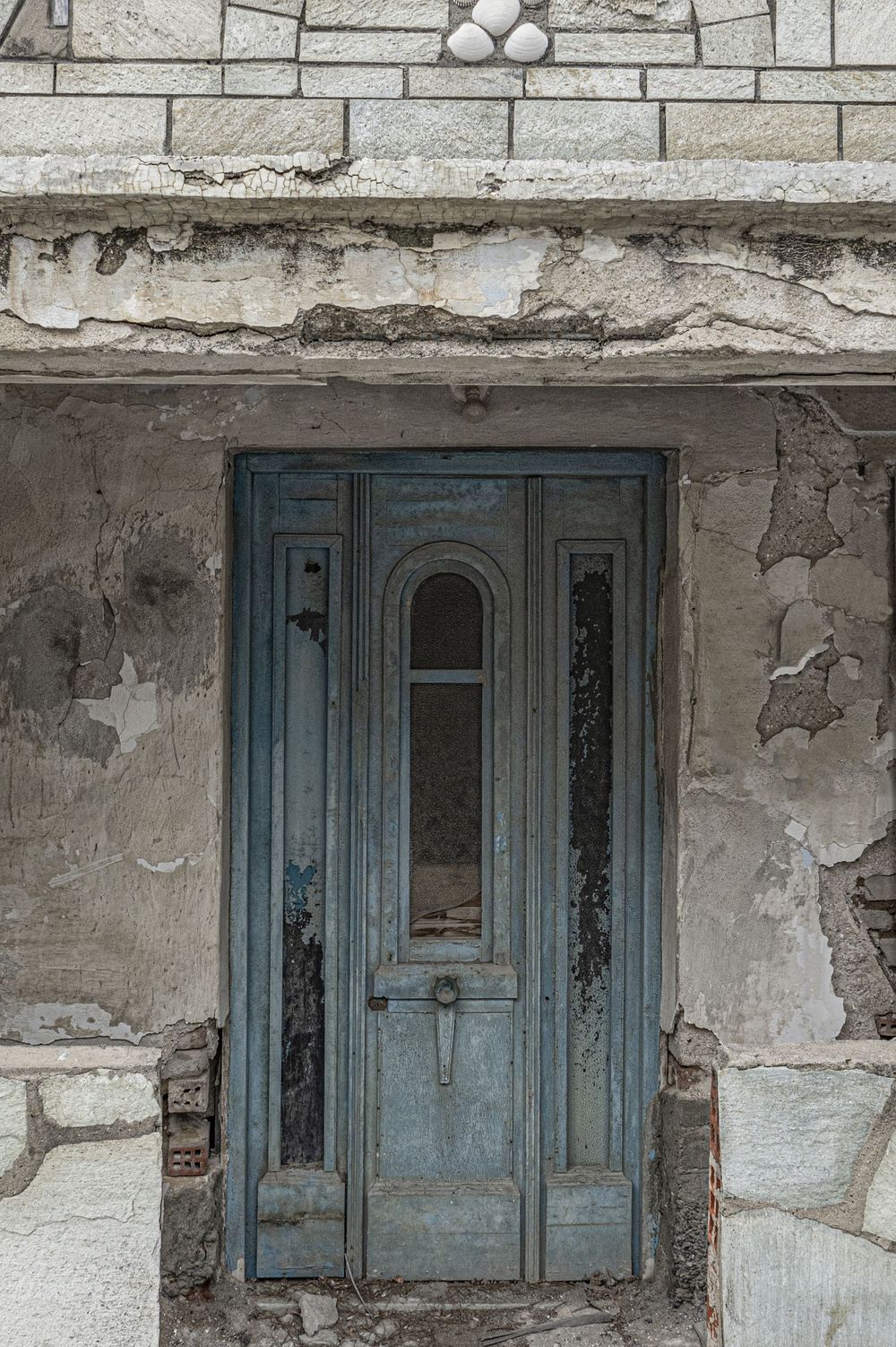 A series of weathered blue shuttered windows on a deteriorating white stucco wall shows architectural decay over time.