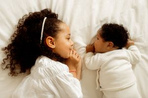 A tender moment of rest on white bedding shows a peaceful scene of shared comfort and curls.