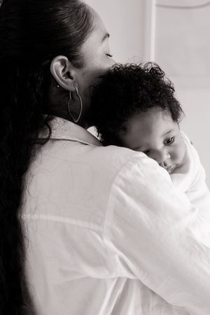 A tender black and white portrait of a parent in a white shirt embracing a small child with curly hair.