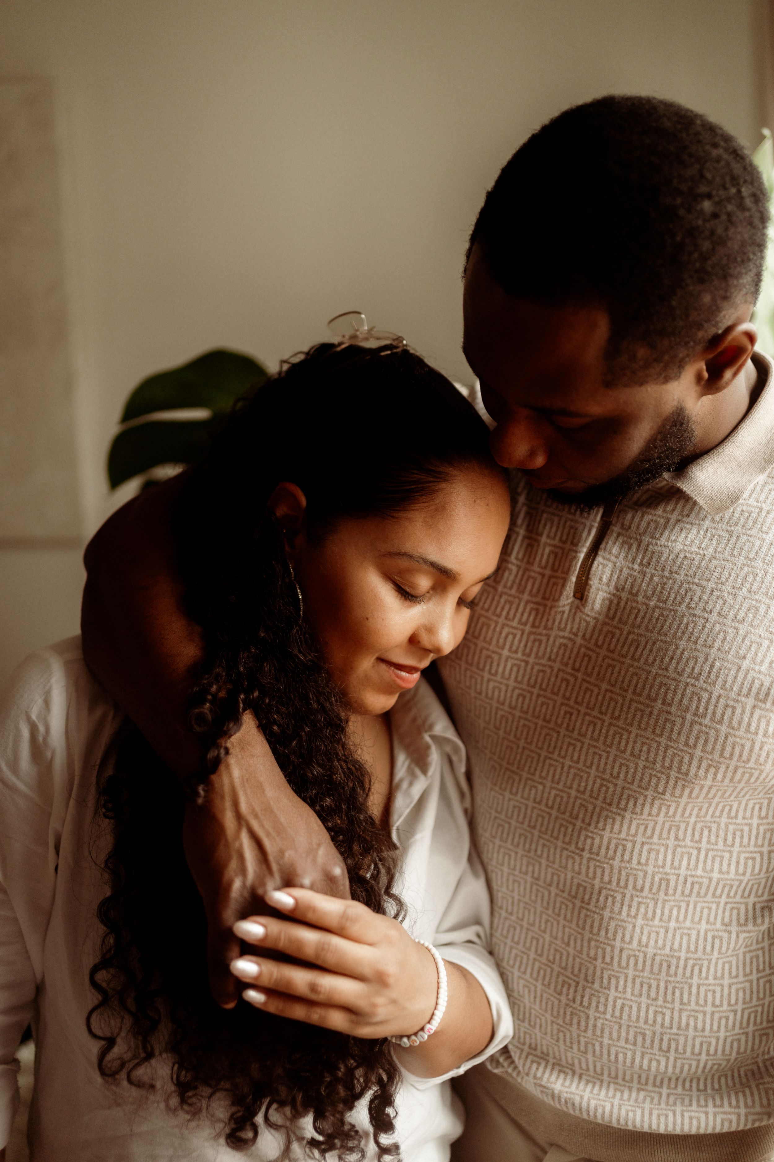 A romantic couple embraces in soft window light while sharing an intimate moment together.