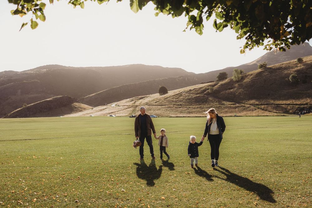 Silhouettes of people walking along a grassy hilltop trail at sunset with golden light in the background.