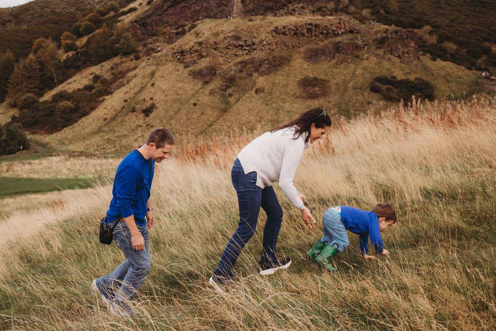 People playing and exploring together on a grassy hillside with brown mountains in the background.