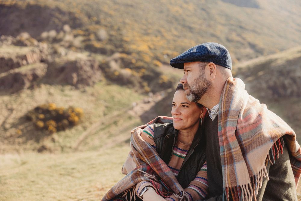 Couple in warm clothing sharing intimate moments while sitting outdoors in a mountainous autumn landscape.