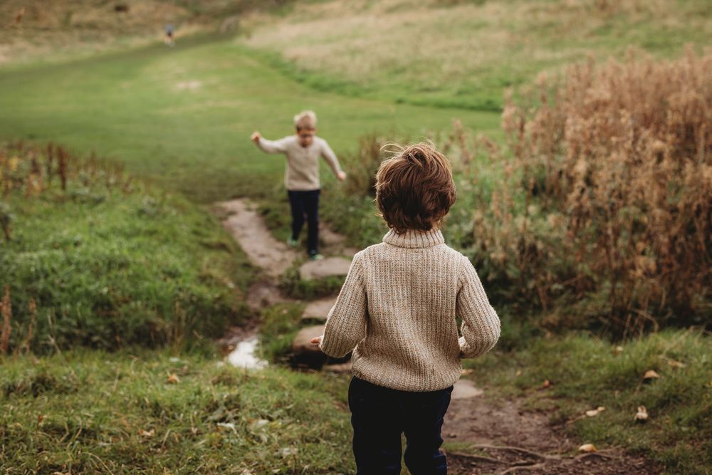 Two people in warm sweaters walking along a winding dirt path through grassy autumn fields.
