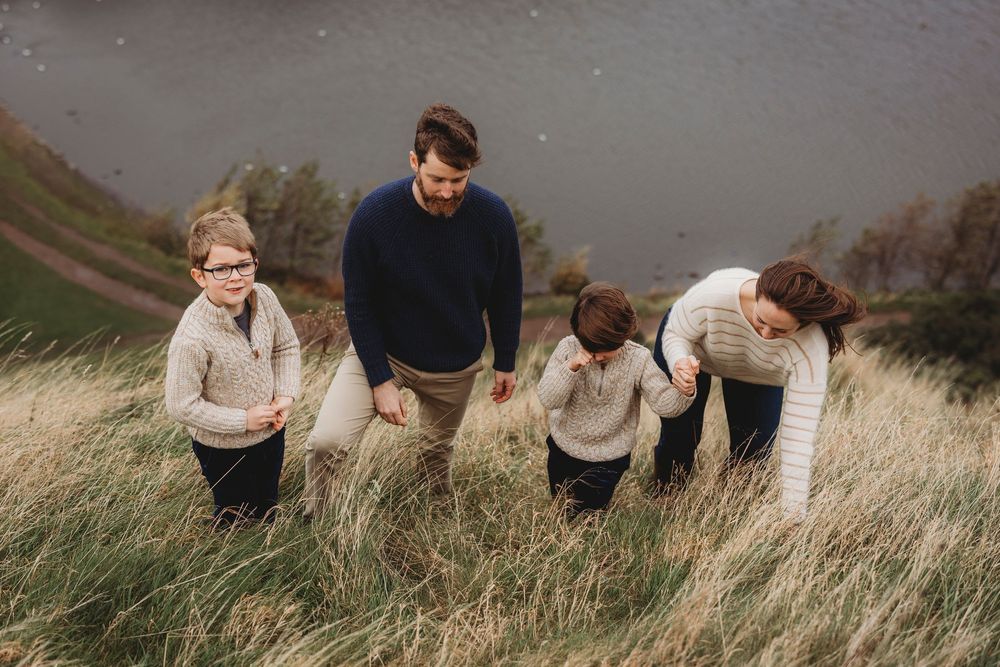 A group of people walking through tall grass on a hillside during an overcast autumn day.