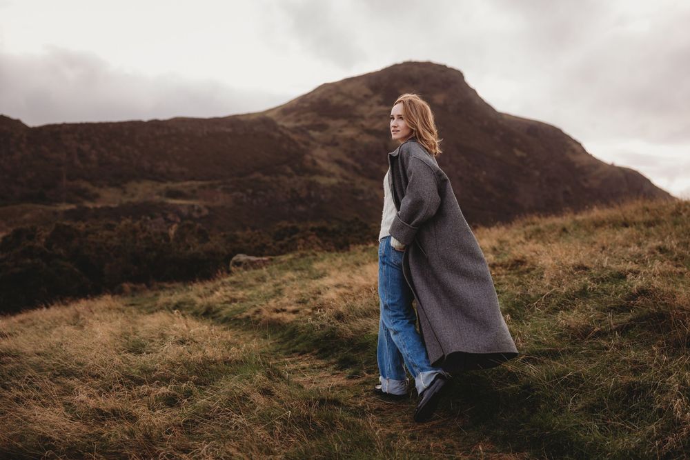 A couple in warm clothing embraces while standing on a scenic mountain overlook on a cloudy autumn day.